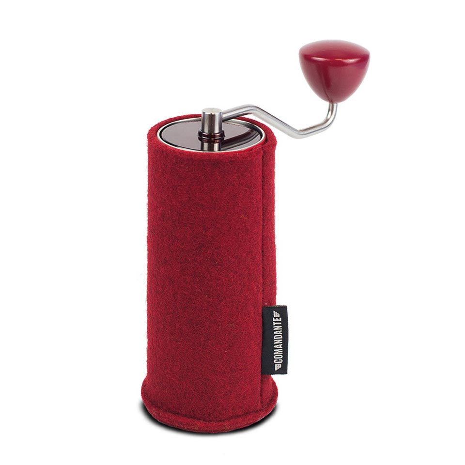 Comandante C40 Kirsebær er en rød manuel kaffekværn med håndsving og filt-filthylster med et lille sort mærke med hvid tekst. Den står oprejst mod en hvid baggrund.