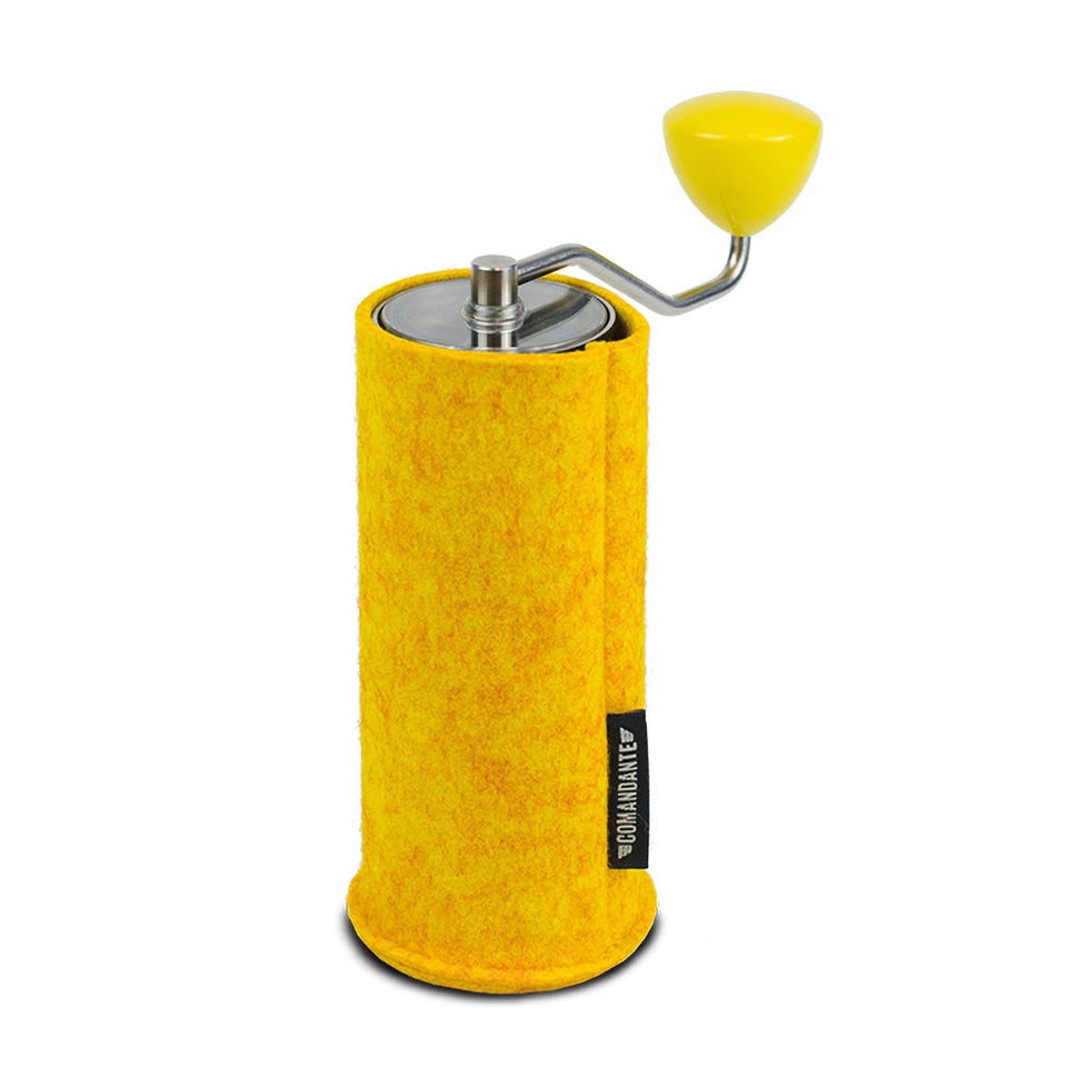 En gul manuel kaffekværn, Comandante C40 Filt Sleeve i Safran, har et håndsving, metaltop og et tekstureret Kashmir-design cover. Mærket "Comandante C40" er tydeligt vist på siden.