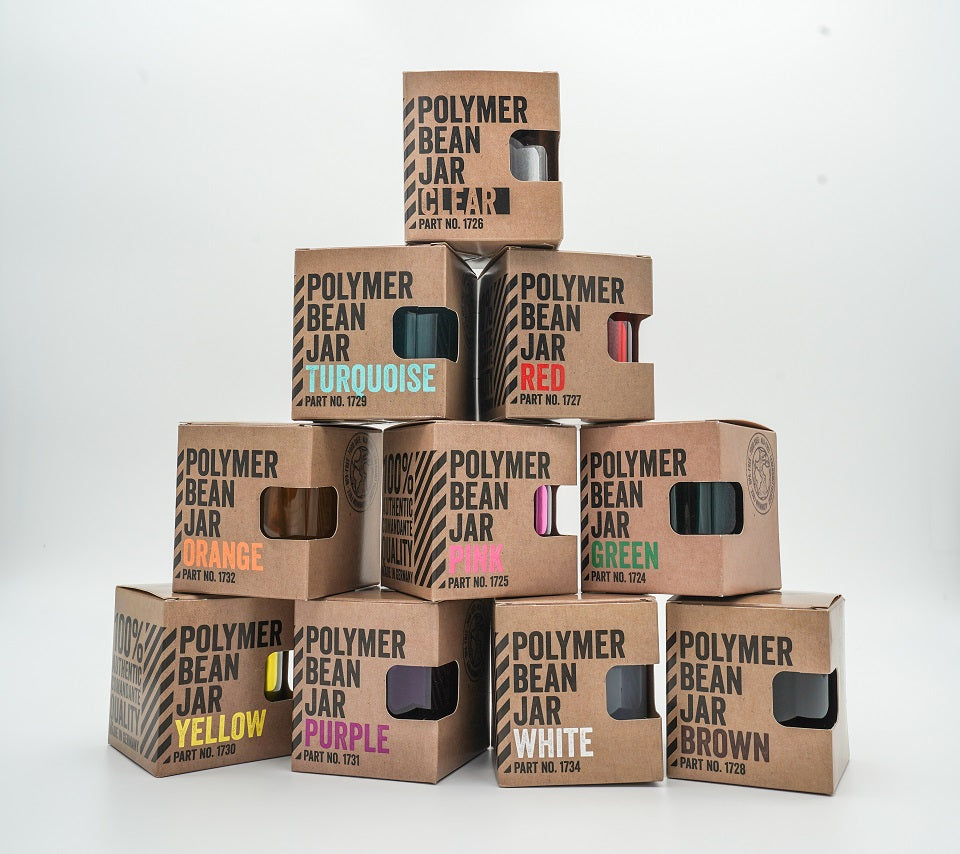 En pyramide af Comandante Polymer Bean Jar-æsker viser et levende udvalg: klar, rød, gul, turkis, orange, pink, lilla, hvid, grøn og brun. Perfekt til din Comandante C40 kværn opsætning. Hver fødevaresikker-boks har et visningsvindue og viser varenummeret.