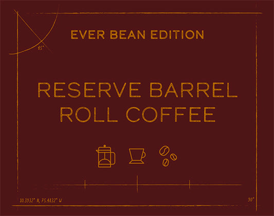 En brun etiket med guldtekst siger "EverBean Limited, Emblematic Barrel Roll (w)." Ikoner af en French press, en kop og tre bønner antyder colombiansk kaffe. Små koordinater og målemærker dekorerer hjørnerne.