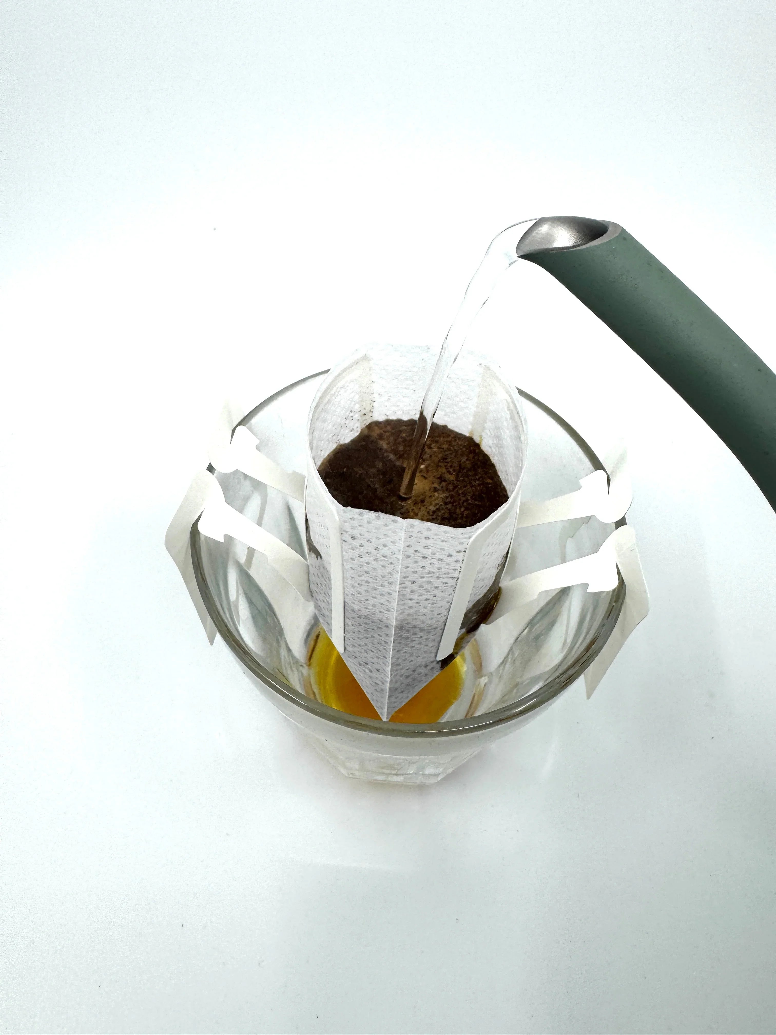Varmt vand hældes i en dryp kaffepose over en glaskop, hvor brygget kaffe samles i bunden.
