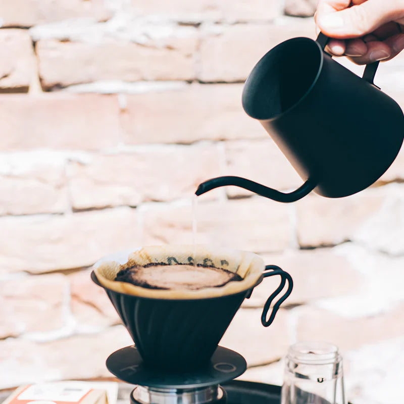 En hvid Braun kaffemaskine med en glaskaraffel, placeret på en træoverflade mod en mørk baggrund. Karaflen har målemærker fra 2 til 10 kopper og sort hank. Strømkablet er synligt på højre side.