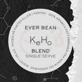 En rund etiket til "Single Serve, KeHo" kaffe fra EverBean ApS. med 100% Arabica Honduras kaffe. Dansk og engelsk tekst vises på en mørk baggrund med en revet højre kant, der fremhæver denne unikke blanding.