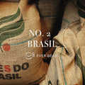 Nærbillede af jutesække mærket "BRASIL" med grøn og rød grafik, der antyder, at de indeholder Single Serve, No. 02 - Brasilen (øko) premium Arabica-bønner fra EverBean ApS. Teksten "NO. 2 BRASIL" og "EVER BEAN" er overlejret.