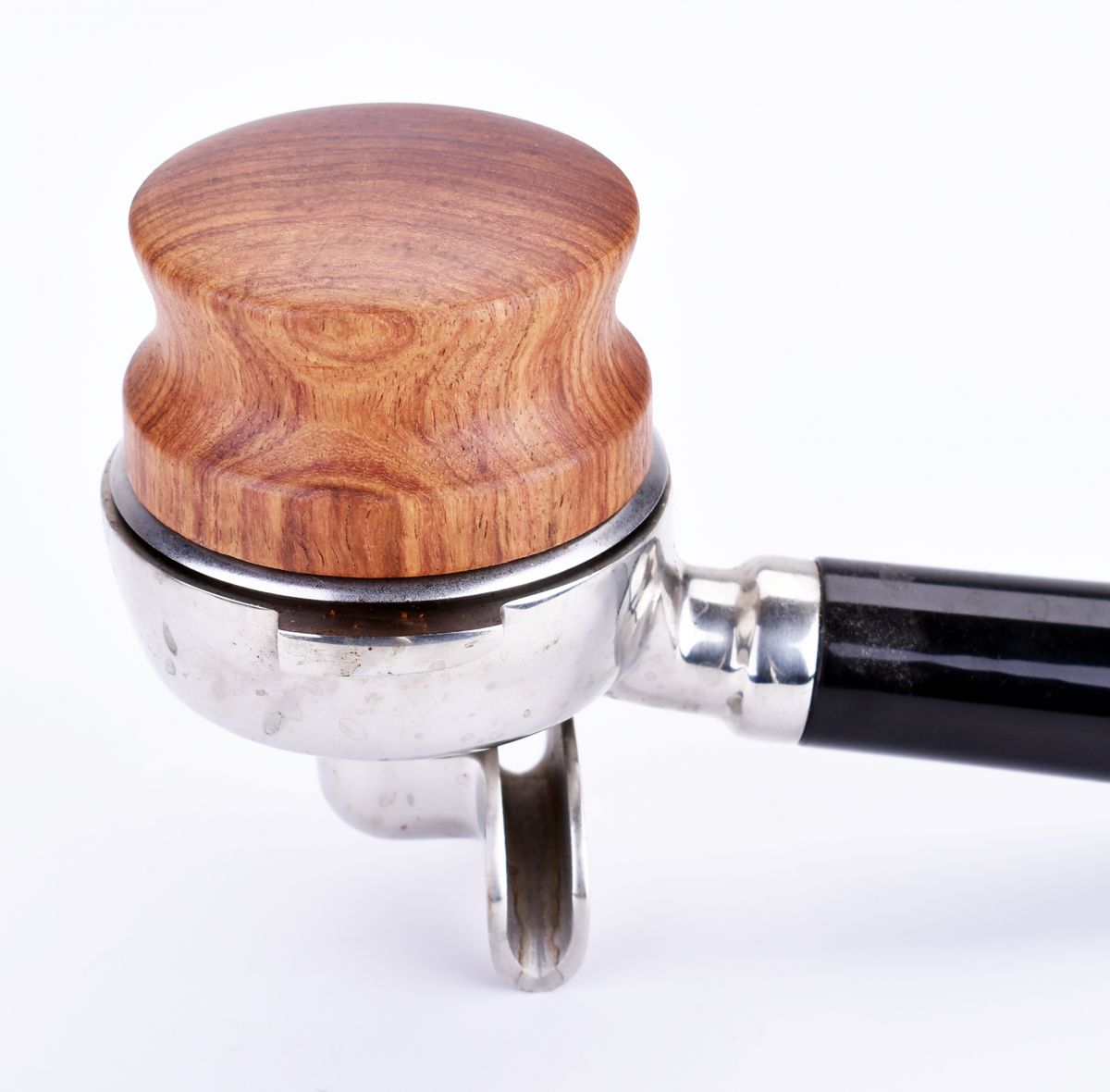 Nærbillede af et portafilter med en skinnende metalbund og træhåndtag, der viser naturlige træårer. Det polerede metal skinner under Joe Frex Coffee Level Tool i Palisander, 58 mm. Baggrunden er almindelig hvid.