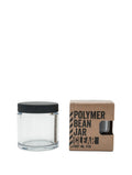 En klar Comandante Polymer Bean Jar med låg, Klar er vist ved siden af en brun æske mærket "Polymer Bean Jar Clear Part No. 1726" med en udskæring, der viser den kompatible krukke til din Comandante C40.