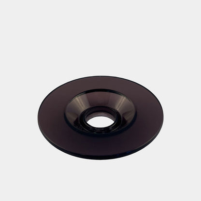 Et blankt, sort glasobjekt fra Comandante, X25 Låg Sort, er donutformet med et centralt cirkulært hul og sat mod en almindelig, lysegrå baggrund.