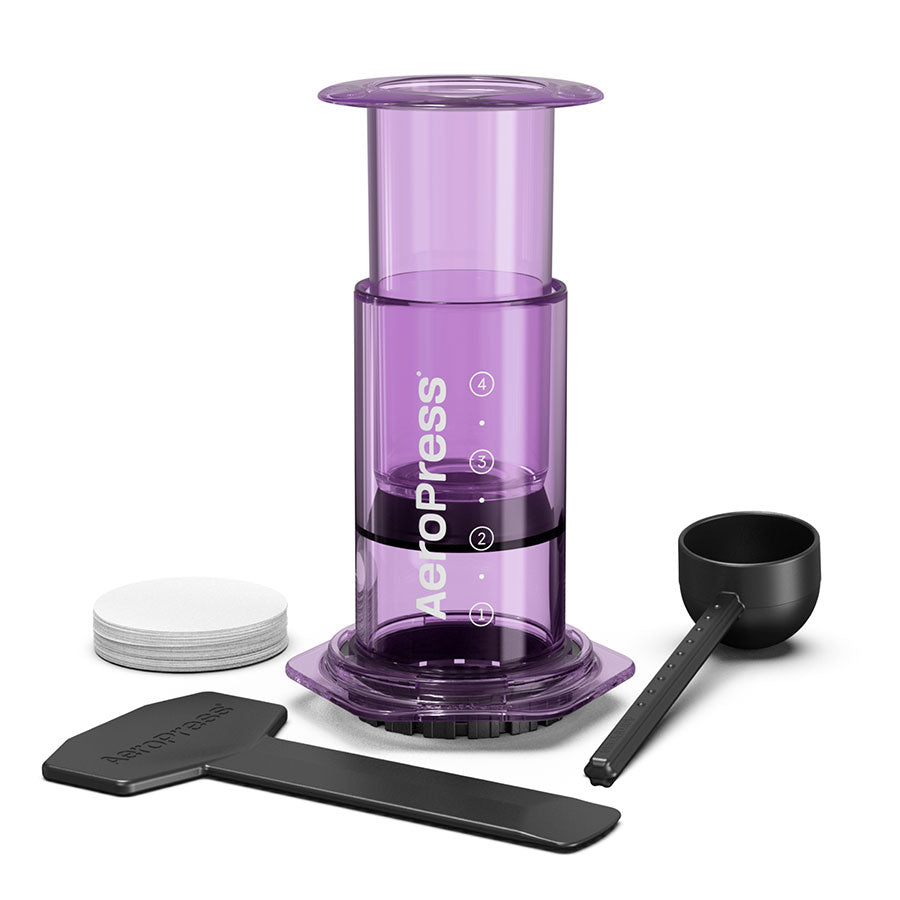 AeroPress Limited Kaffebrygger fra Aeropress i lilla, med scoop, omrører og papirfiltre, har innovativ bryggeteknologi og er pænt præsenteret på en hvid baggrund.