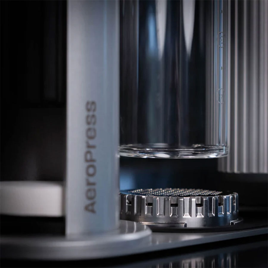 Nærbillede af Aeropress Premium Organizer fra Aeropress, der fremviser dens minimalistiske design og cylindriske kammer over et filter i rustfrit stål, med Aeropress-logoet synligt. Billedet fremhæver bryggemaskinens elegante komponenter.