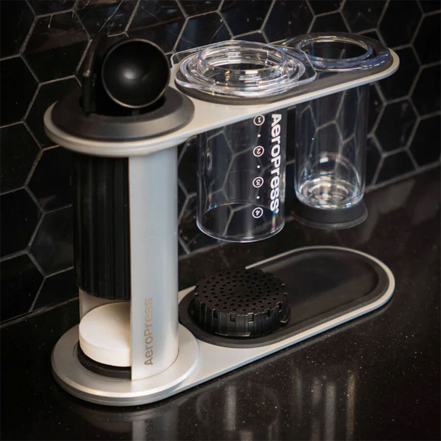 Aeropress Premium Organizer fra Aeropress har et minimalistisk design, der pænt opbevarer din ske, stempel, padle og bryggekamre på en elegant sort bordplade mod en sekskantet flisebagplade.