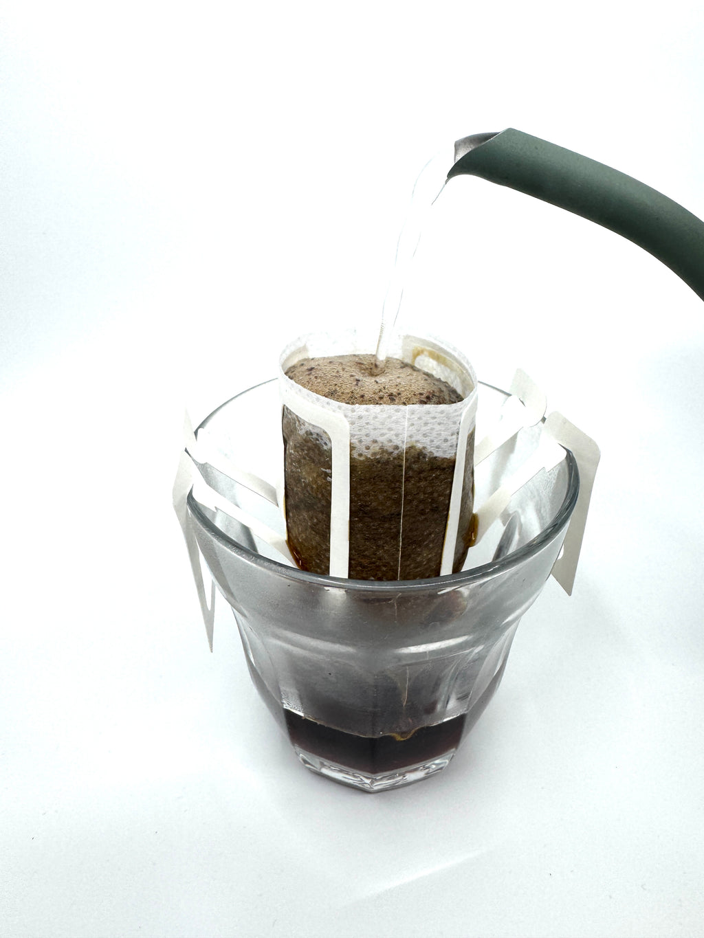 EverBean ApS. No. 04 - Colombia, Øko, Decaf, Single Serve kaffefilter sættes på et glas, og varmt vand hældes fra en kedel over kaffegrumset for at få en frisk brygning.