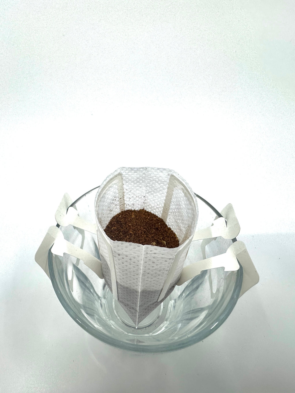 Et No. 11 - Kenya, Single Serve drypkaffefilter fra EverBean ApS. hviler på en klar glaskop, hvor papirarmene holder den åben - klar til en perfekt single serve-bryggeoplevelse.