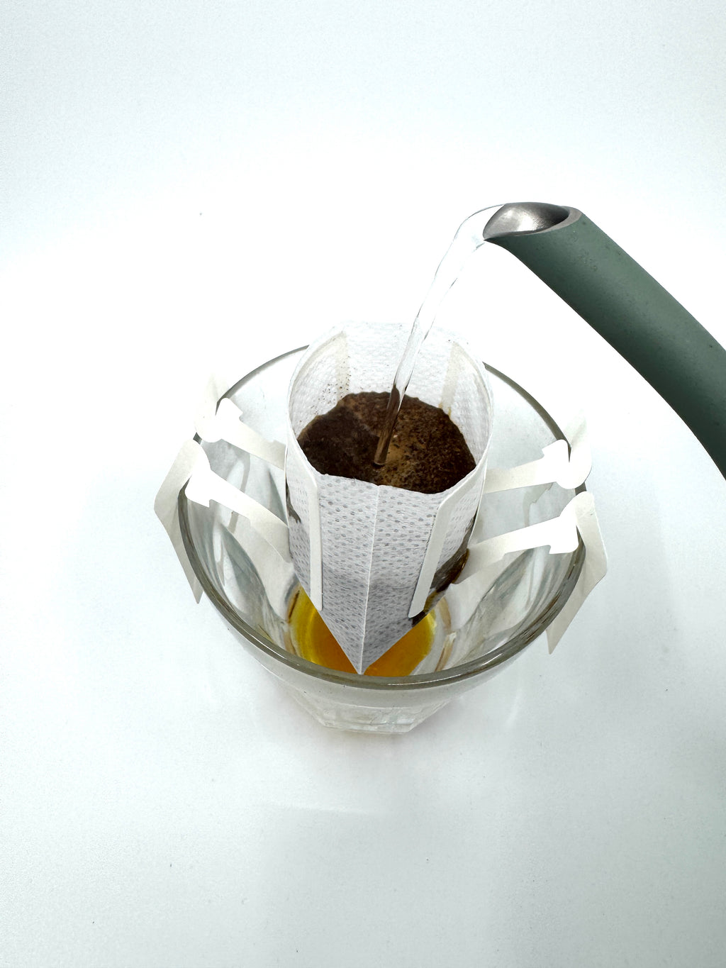 En kedel hælder varmt vand over No. 02 - Brasilen, Øko, Single Serve fra EverBean ApS. og lader frisk økologisk brasiliansk kaffe brygge i et drypfilter oven på en glaskop.