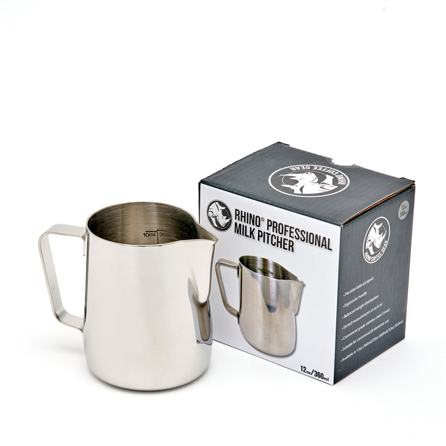 En Rhino Coffee Gear Pro Milk Pitcher står ved siden af æsken, som viser produktnavnet "Rhino Coffee Gear, Pro Milk Pitcher", et billede af kanden i rustfrit stål og Rhino Coffee Gear-logoet.