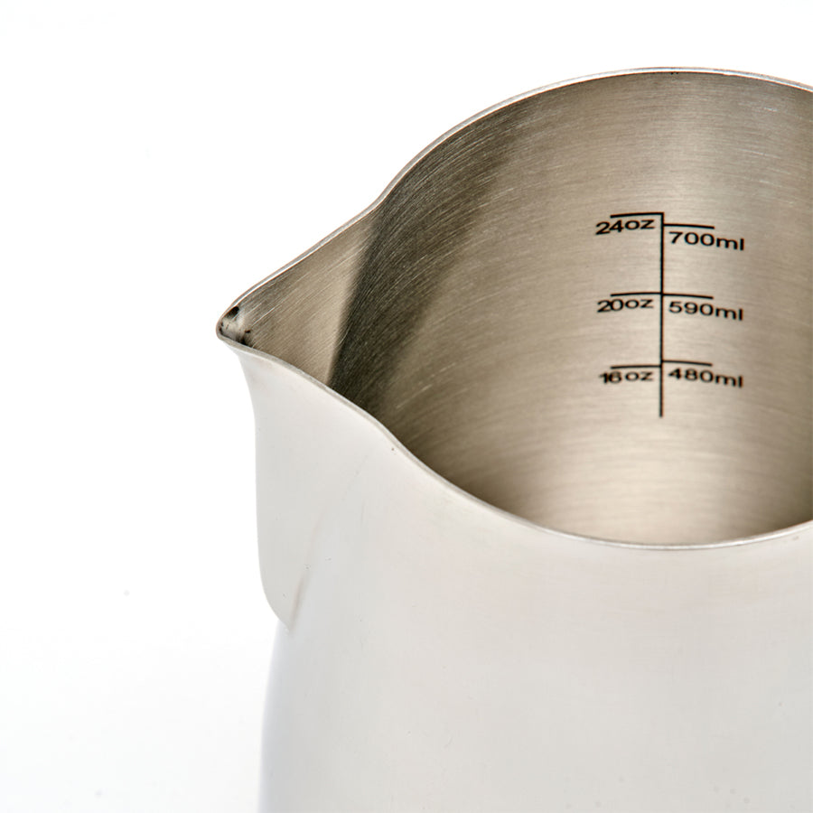 Et nærbillede af Rhino Coffee Gear Pro Milk Pitcher - rustfrit stål med måleangivelser i ounces og milliliter på den indvendige væg samt en tud i venstre side.