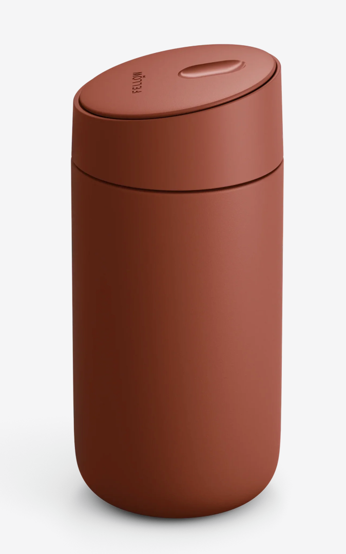Et mat, cylindrisk, rødbrunt Fellow Carter Slide Mug (Termo Krus) med keramisk belægning og et matchende låg med en lille oval fordybning og en subtil tekst på en hvid baggrund.