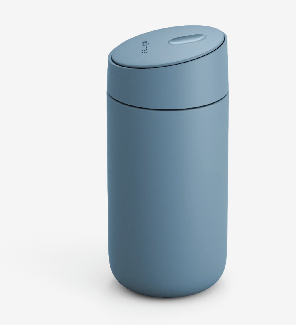 Et elegant, matblåt Fellow Carter Slide Mug termo krus med en afrundet krop og et ovalt låg med en keramisk belægning på en ensfarvet hvid baggrund.