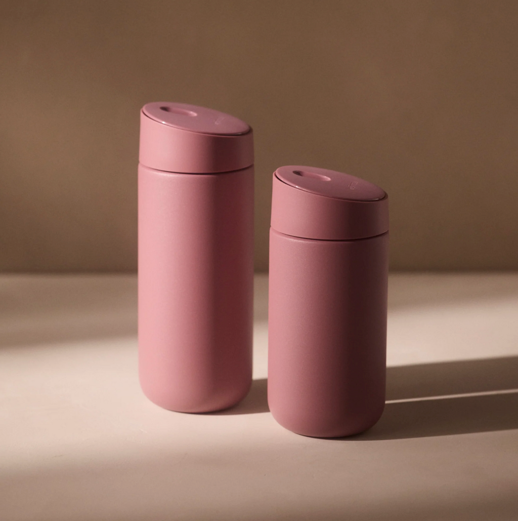 To Fellow Carter Slide Mug Termo Krus i mat rosa med afrundede låg står side om side på en beige overflade, blødt oplyst. Hvert Fellow-krus har keramisk belægning for varig kvalitet mod en neutral baggrund.