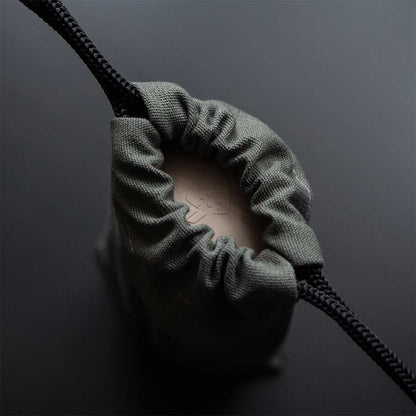 Comandante Toolbag #5 er en kompakt, mørk pose med snoretræk fremstillet af struktureret bomuldslærred, som er delvist åben for at vise en brunlig genstand indeni - ideel til opbevaring af dit kaffeudstyr fra Comandante.