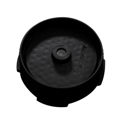 Et nærbillede af AeroPress Flow Control Filter Cap fra Aeropress med et centralt cirkulært filterområde og teksturerede sider fremhæver dette vigtige tilbehør på en hvid baggrund.