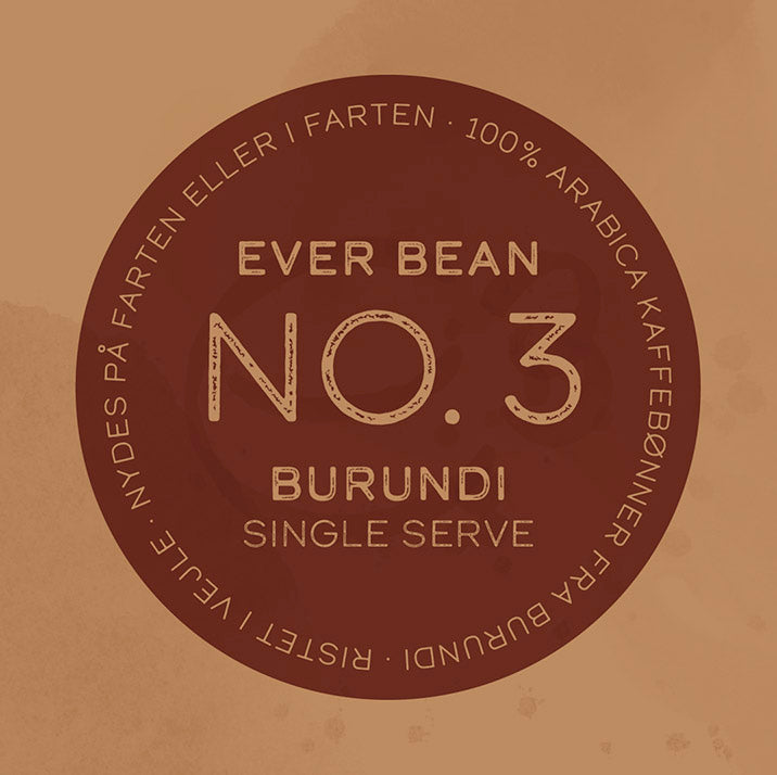 En rund, brun kaffemærkat med teksten: »Nr. 3 · Burundi · Single Serve Drip Bag.« Langs kanten: »100 % Arabica-kaffebønner fra Burundi. Ristet i julen. Nydes som lys filterkaffe eller pour over på farten.“ Mærke: EverBean ApS.