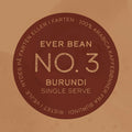 En rund, brun kaffemærkat med teksten: »Nr. 3 · Burundi · Single Serve Drip Bag.« Langs kanten: »100 % Arabica-kaffebønner fra Burundi. Ristet i julen. Nydes som lys filterkaffe eller pour over på farten.“ Mærke: EverBean ApS.
