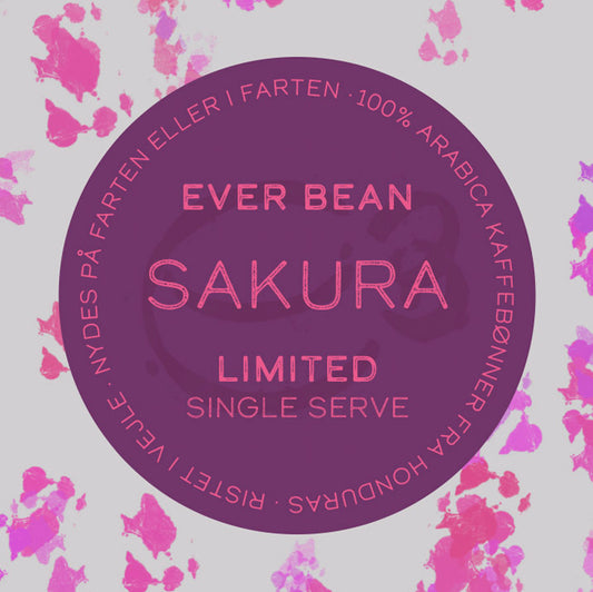 På en rund etiket med pink og lilla stænk står der: "EverBean Limited Single Serve, Sakura". Nyd praktisk single-serve kaffe lavet af 100% Arabica sakura-bønner fra Honduras, ristet i Viborg - perfekt til kaffe på farten.